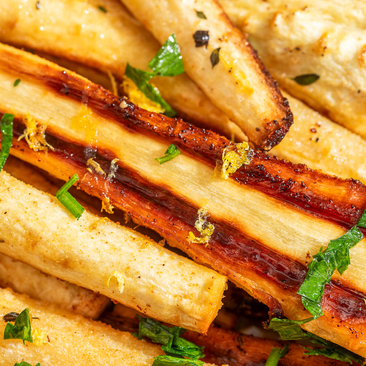Close up image of golden caramelized roasted parsnips garnished with fresh green herbs and lemon zest.
