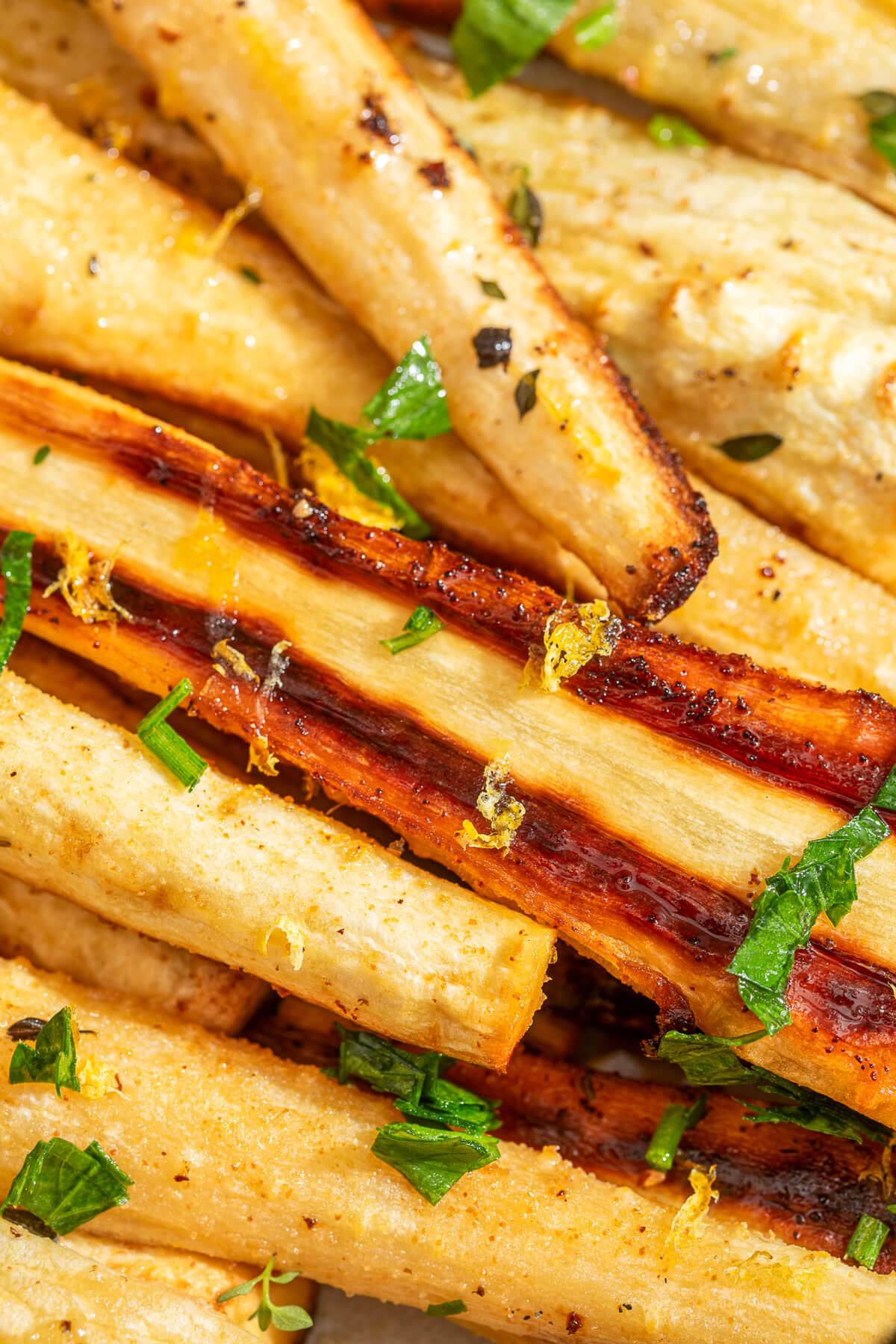 Close up image of golden caramelized roasted parsnips garnished with fresh green herbs and lemon zest.