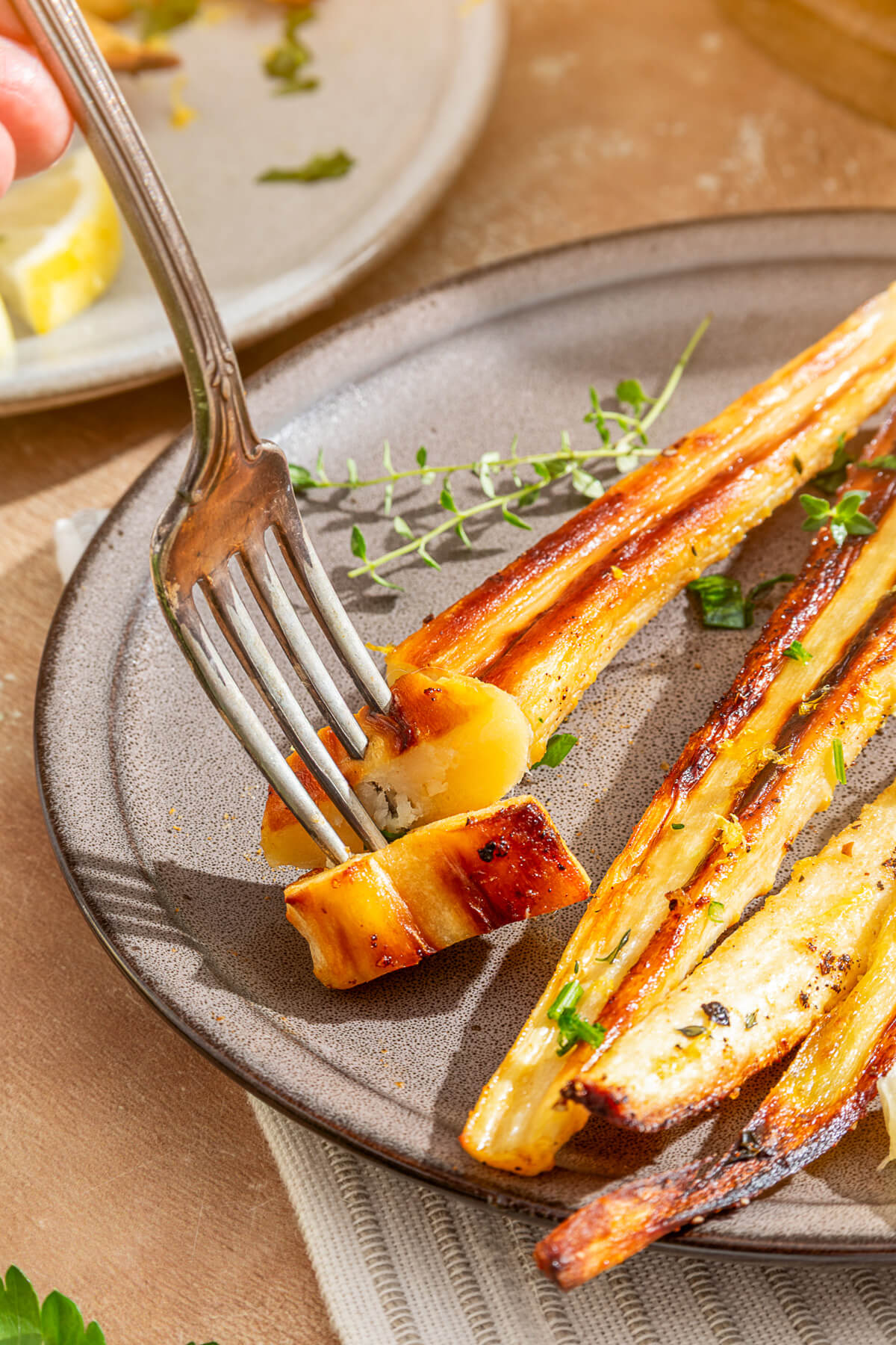 A fork holds a piece of roasted parsnip on a dinner plate full of roasted parsnips.