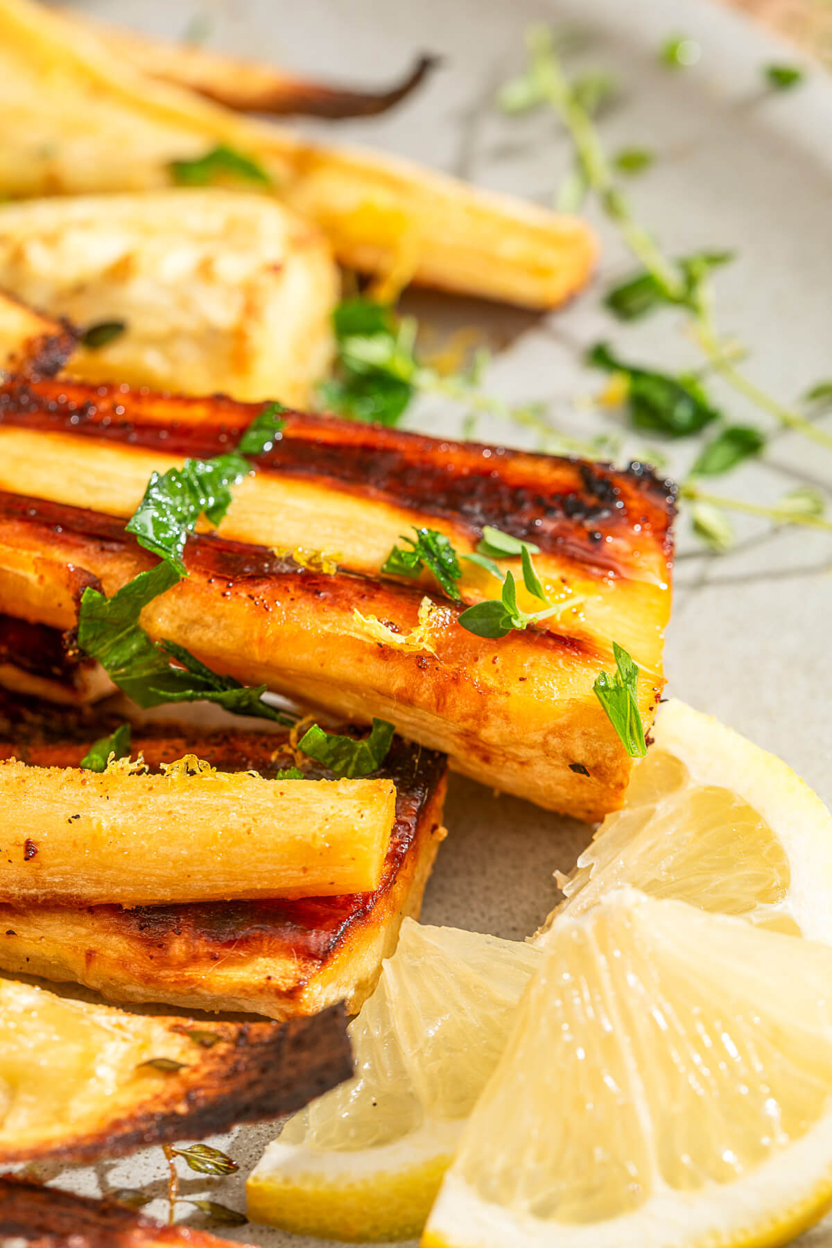Close up image of golden caramelized roasted parsnips garnished with fresh green herbs and lemon zest.
