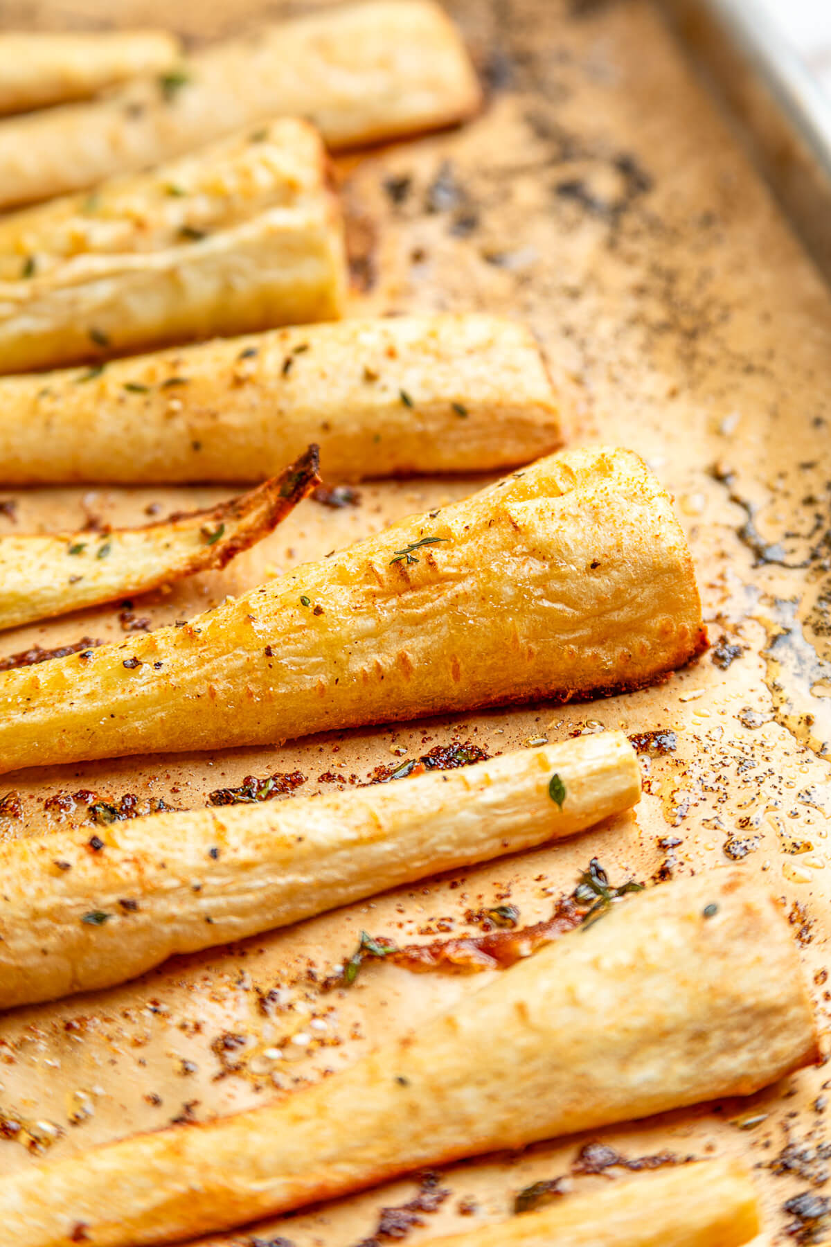 Close up image of golden caramelized roasted parsnips on a baking sheet.