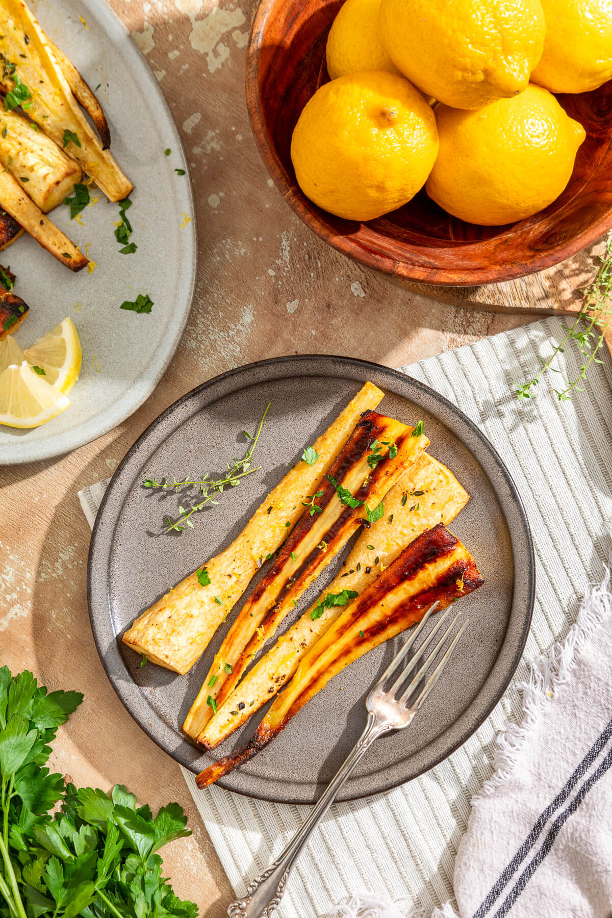 A dinner plate containing golden caramelized roasted parsnips garnished with fresh green herbs and lemon zest on a dinner table.