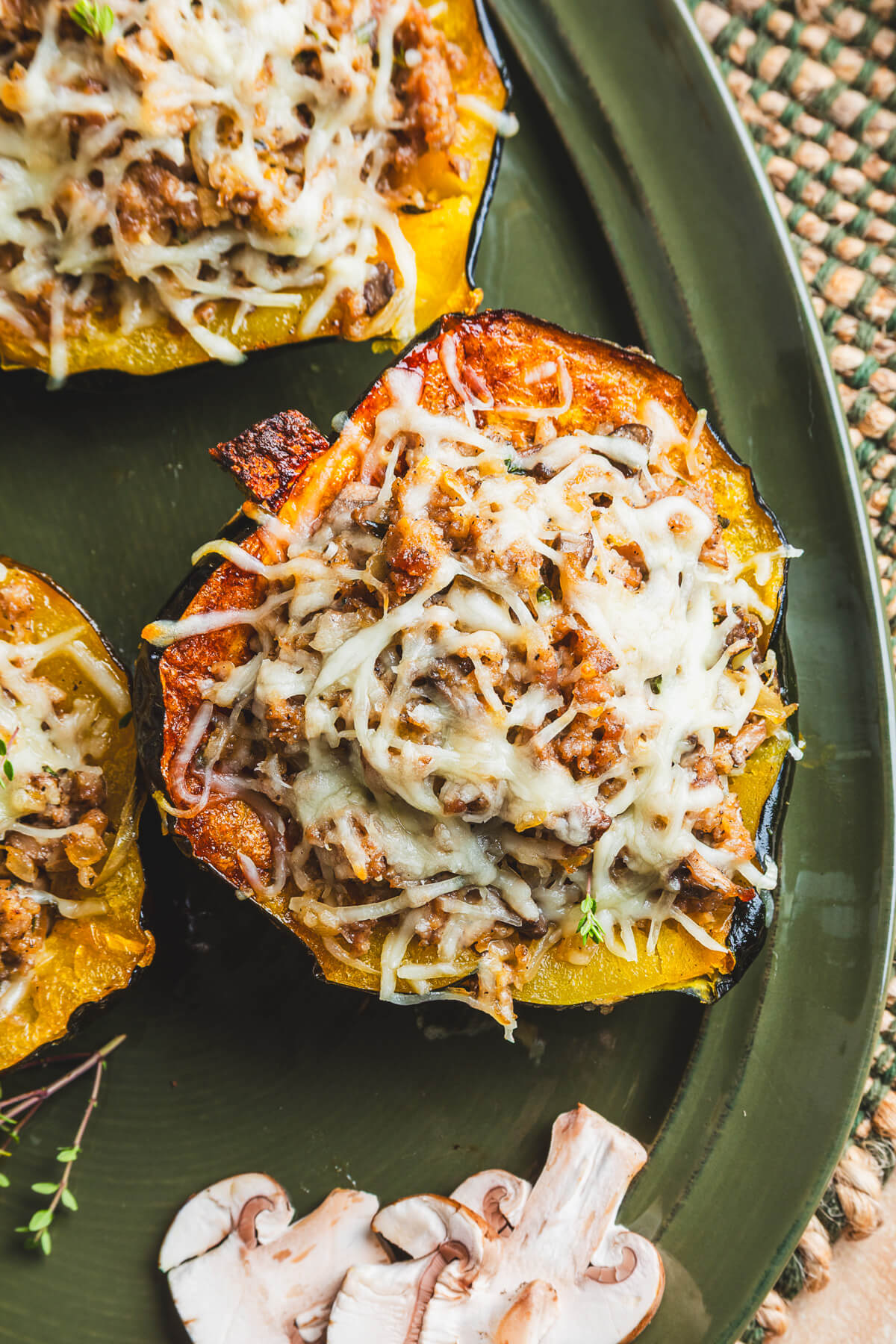 Three halves of roasted acorn squash stuffed with sausage filling and topped with melted mozzarella cheese on a green platter.