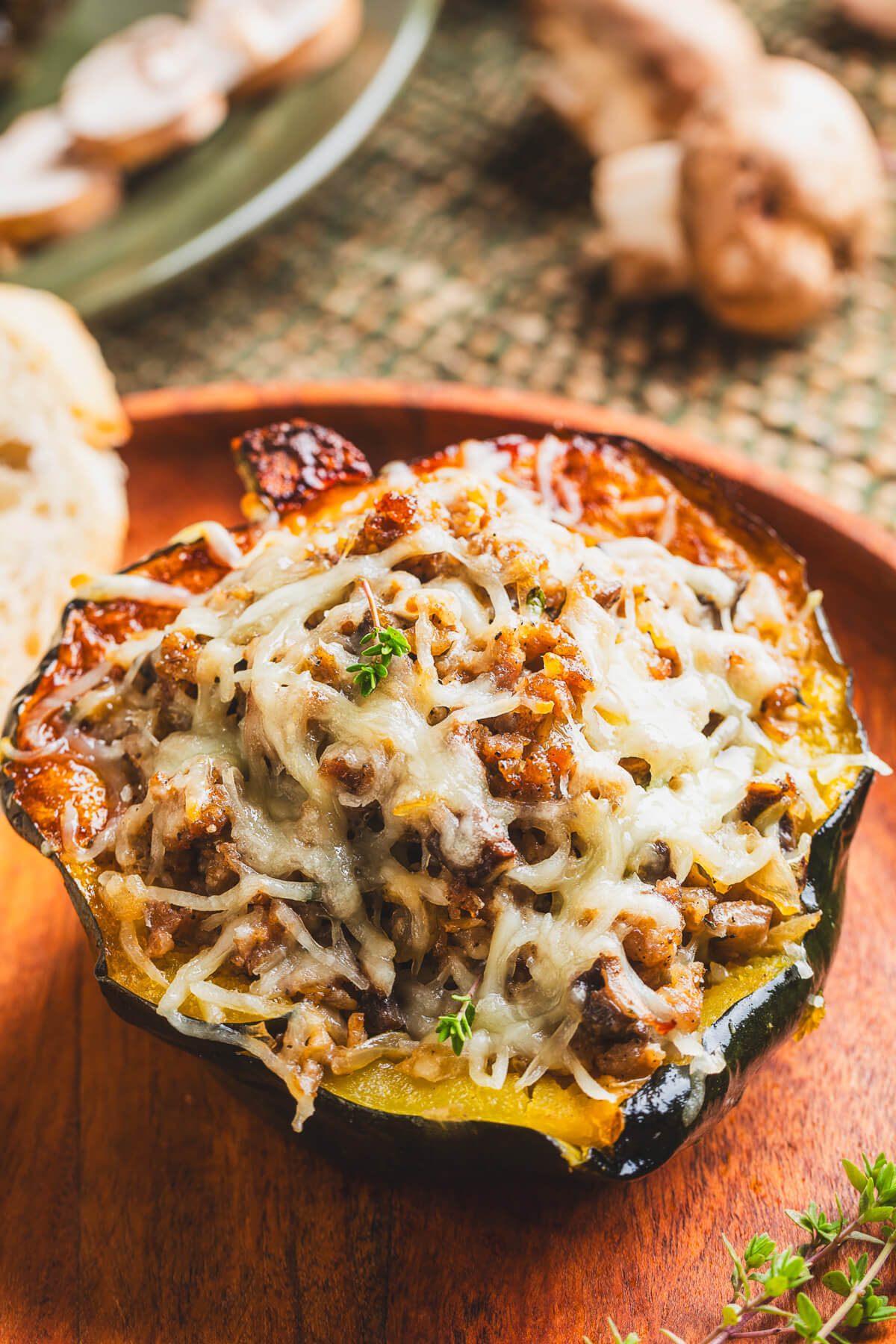 One half of a roasted acorn squash stuffed with sausage filling and topped with melted mozzarella cheese on a wooden plate.
