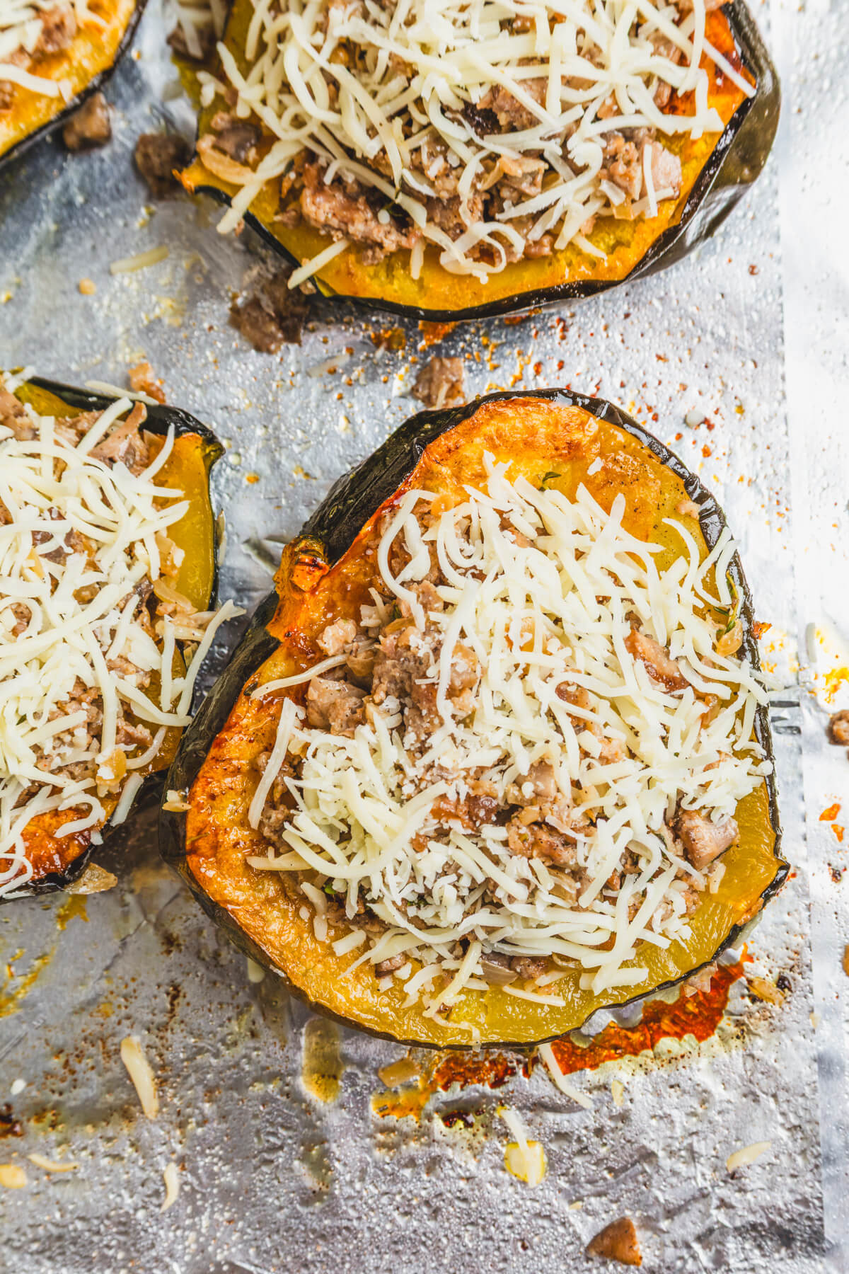 Four halves of roasted acorn squash stuffed with sausage filling and topped with melted mozzarella cheese on a baking sheet.