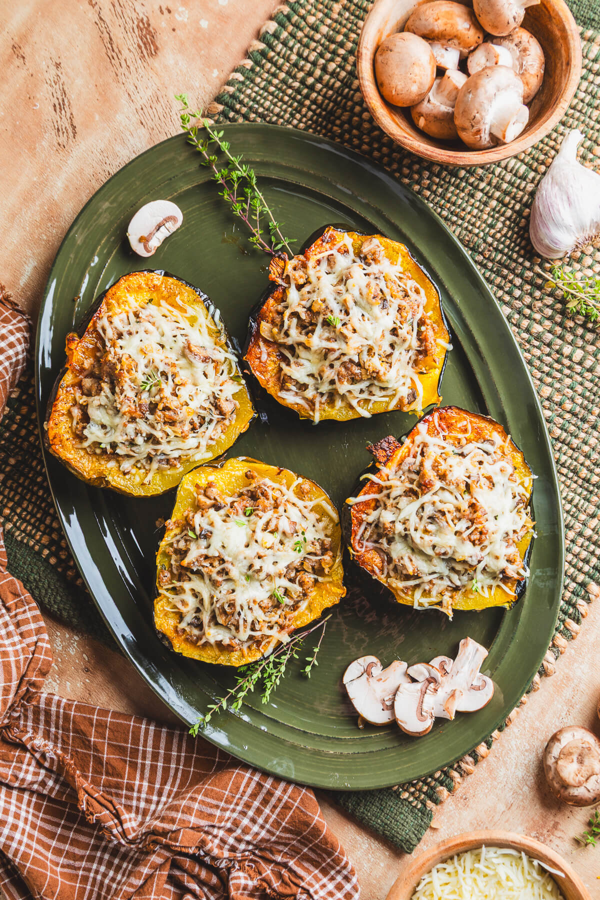 Four halves of roasted acorn squash stuffed with sausage filling and topped with melted mozzarella cheese on a green platter.