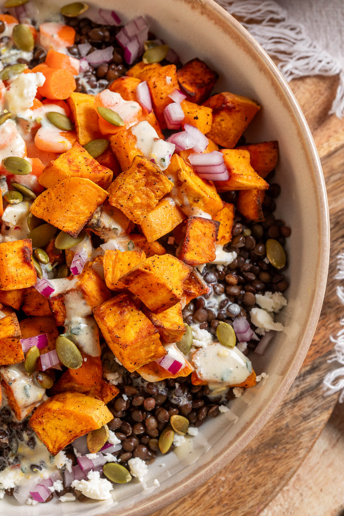 A vibrant orange Sweet Potato Lentil Bowl topped with feta cheese, and toasted pepitas.