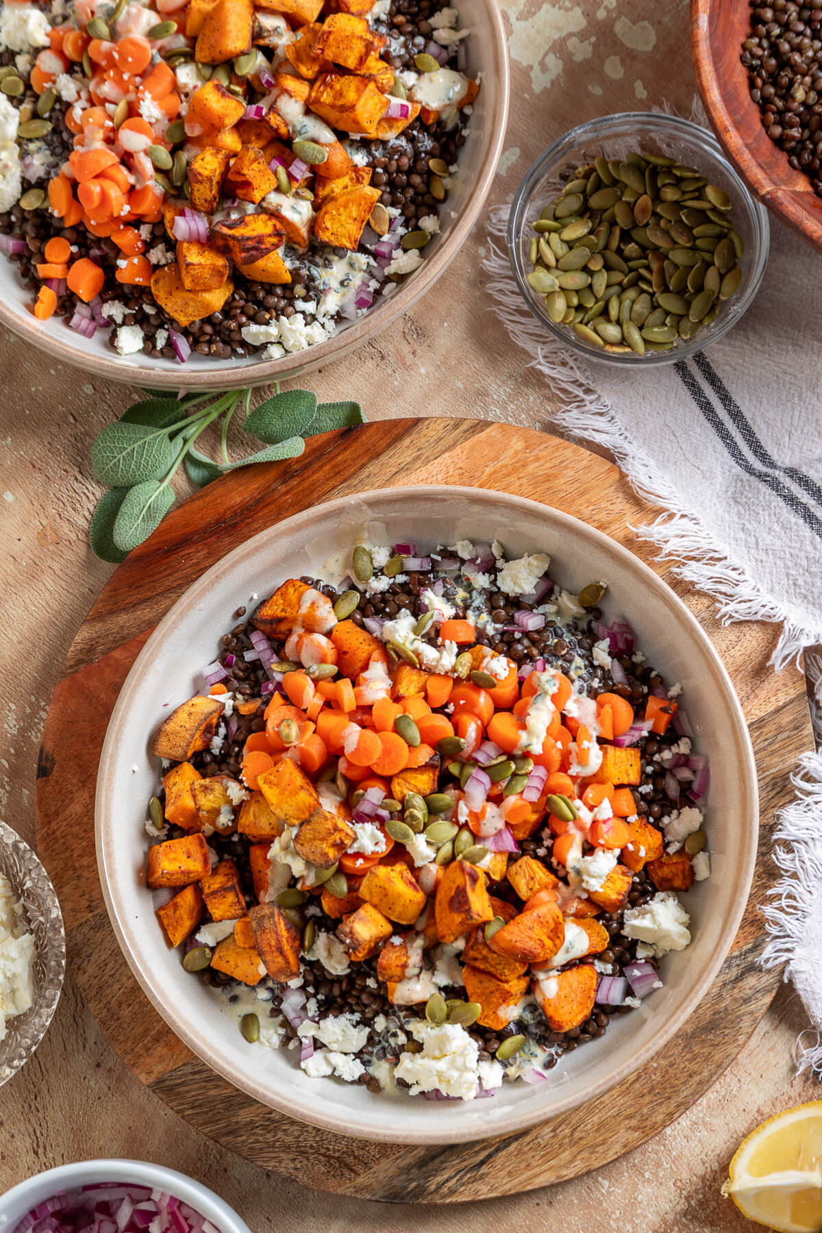 Two vibrant orange Sweet Potato Lentil Bowls topped with feta cheese, and toasted pepitas on a dining table.