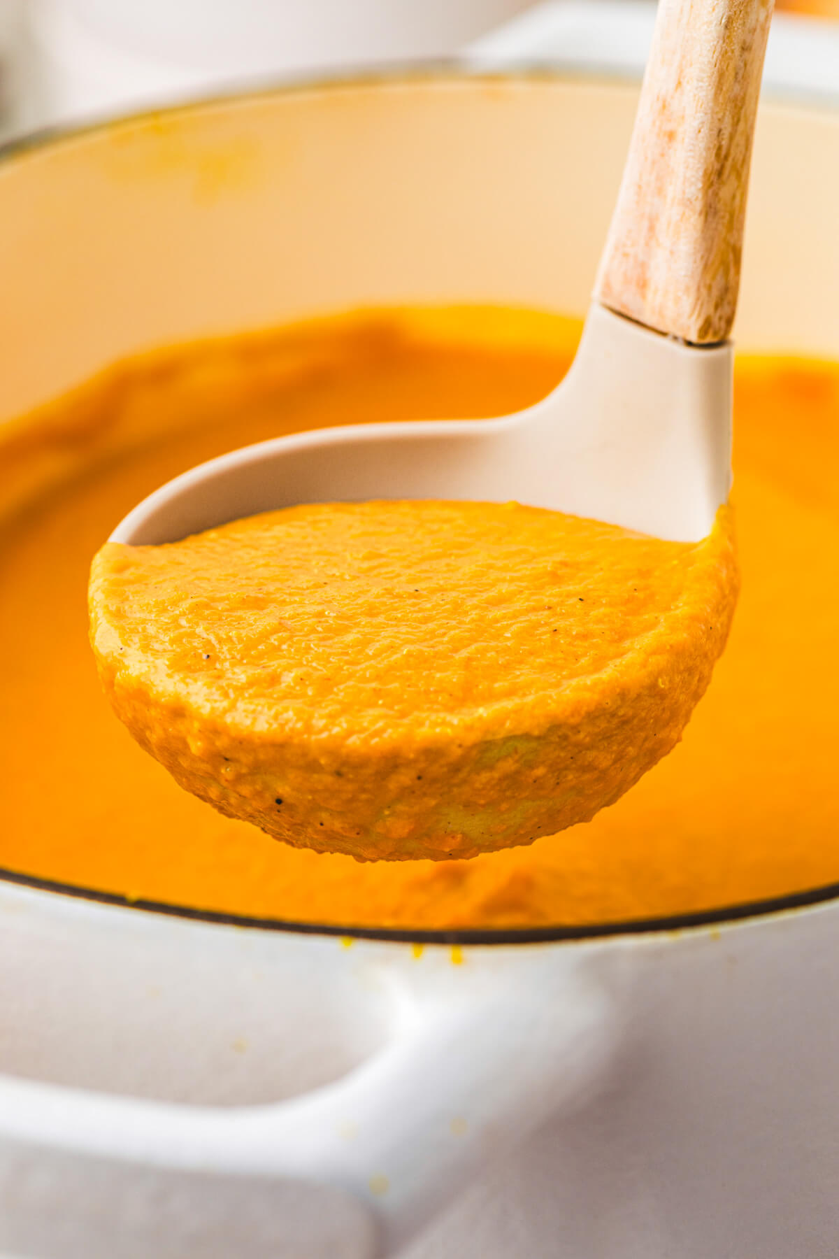 A soup ladle full of vibrant orange carrot lentil soup over the soup pot.