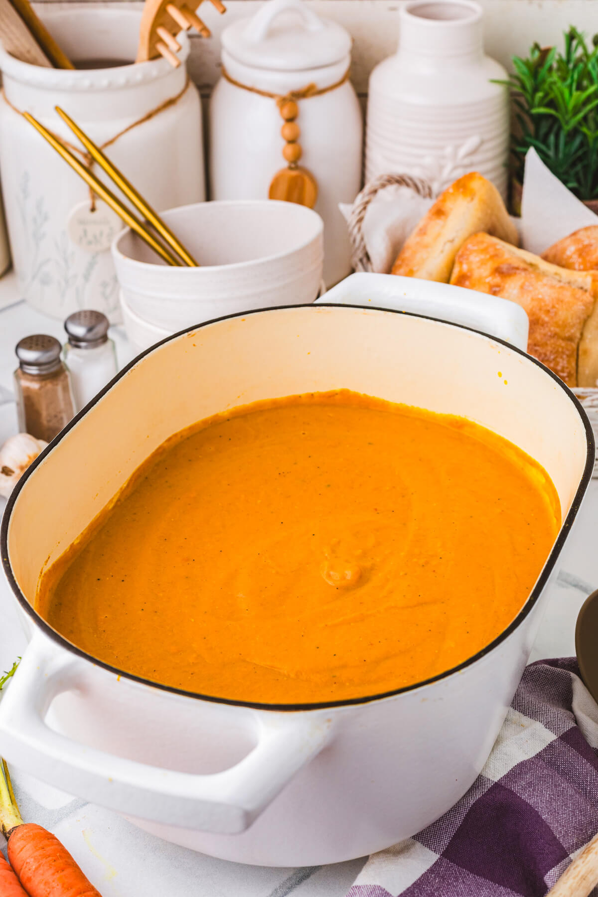 A large oval soup pot filled vibrant orange carrot lentil soup surrounded by soup ingredients.