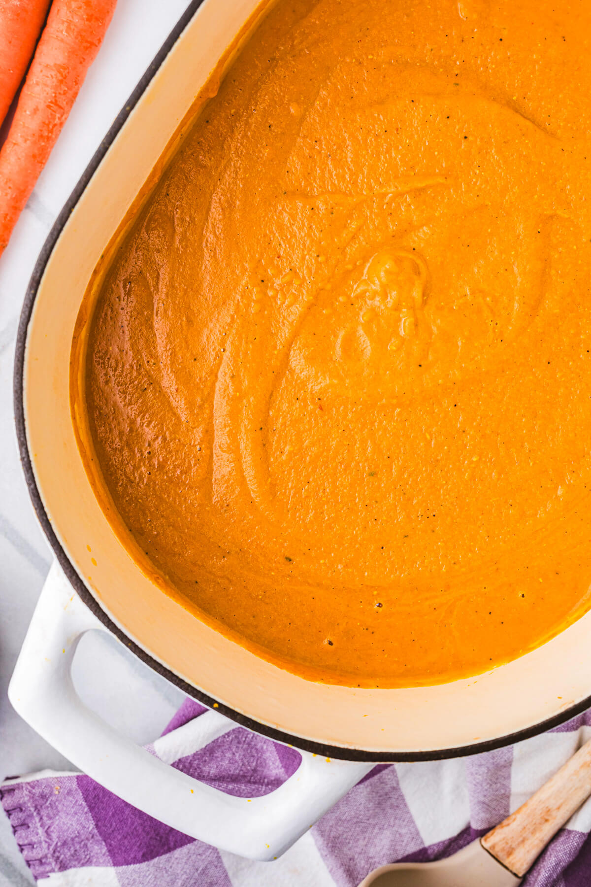 A large oval soup pot filled vibrant orange carrot lentil soup surrounded by soup ingredients.