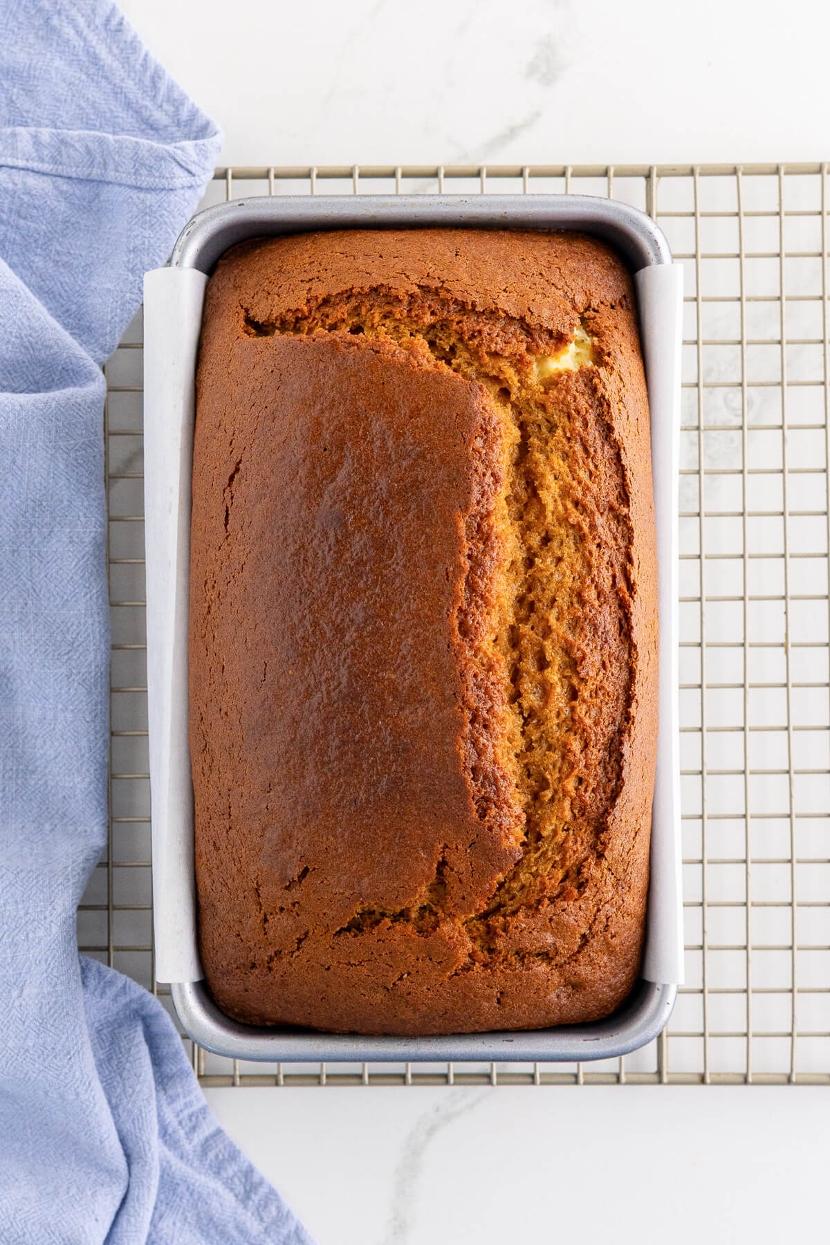 One whole quick bread cooling in a baking pan on a wire rack.