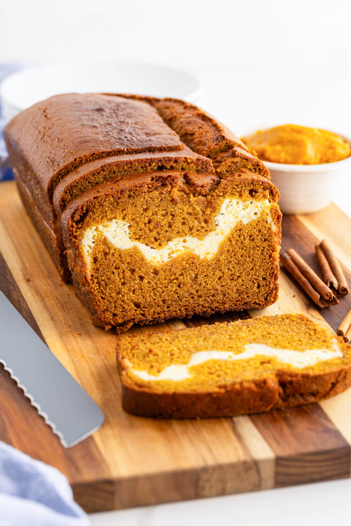 A cream cheese pumpking loaf on a wooden cutting board with one slice sliced off showing the cream cheese swirl.