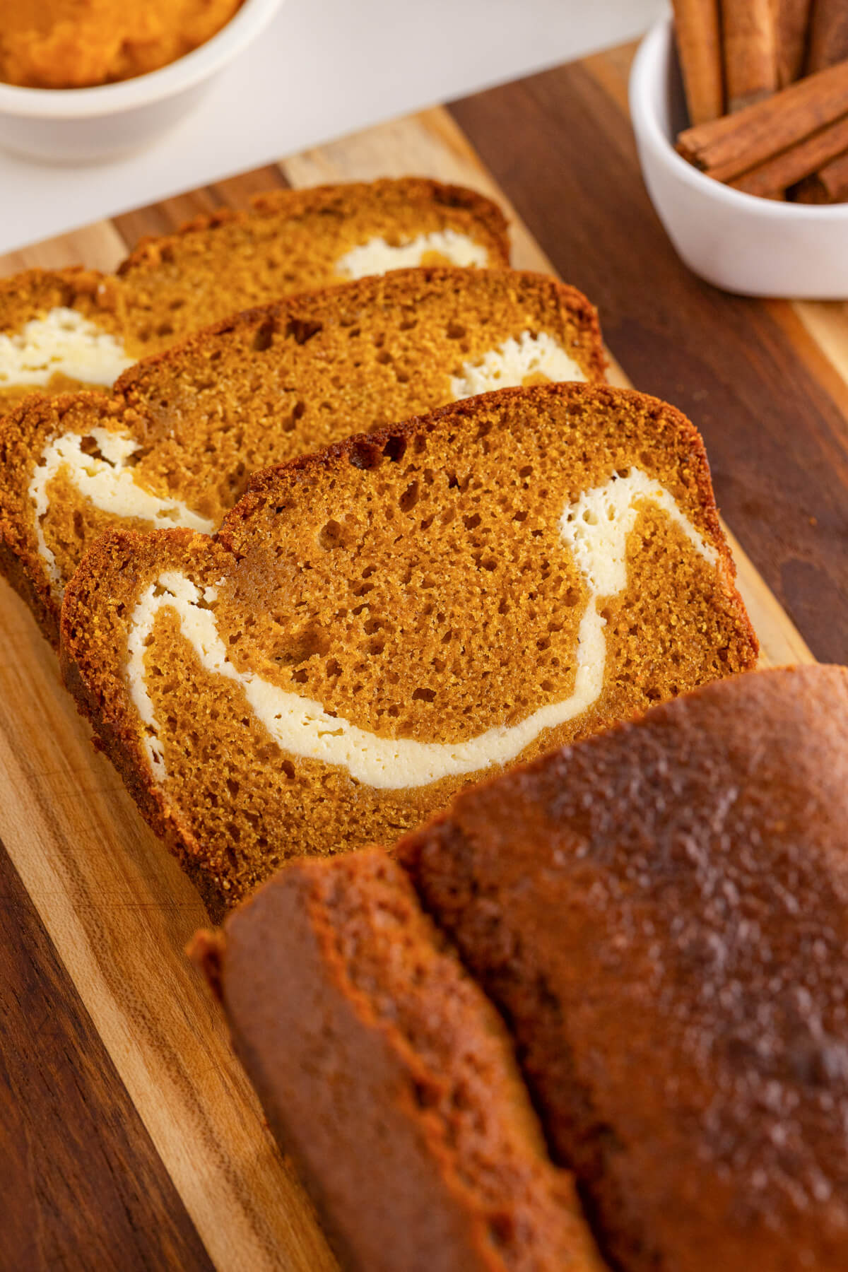 A cream cheese pumpking loaf on a wooden cutting board with three slices sliced off showing the cream cheese swirl.