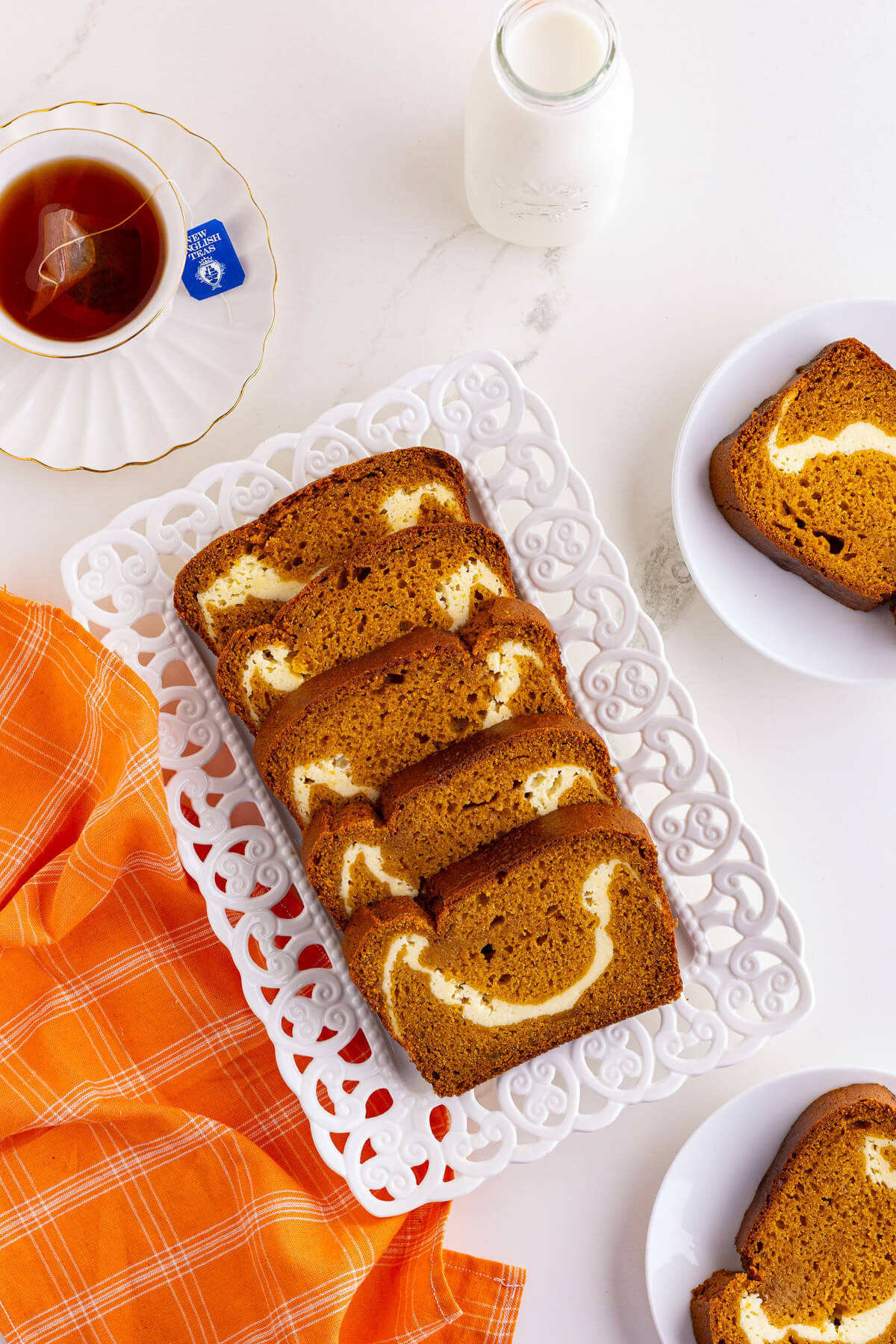 Five slices of orange pumpkin bread with a cream cheese layer in a square vintage plate.