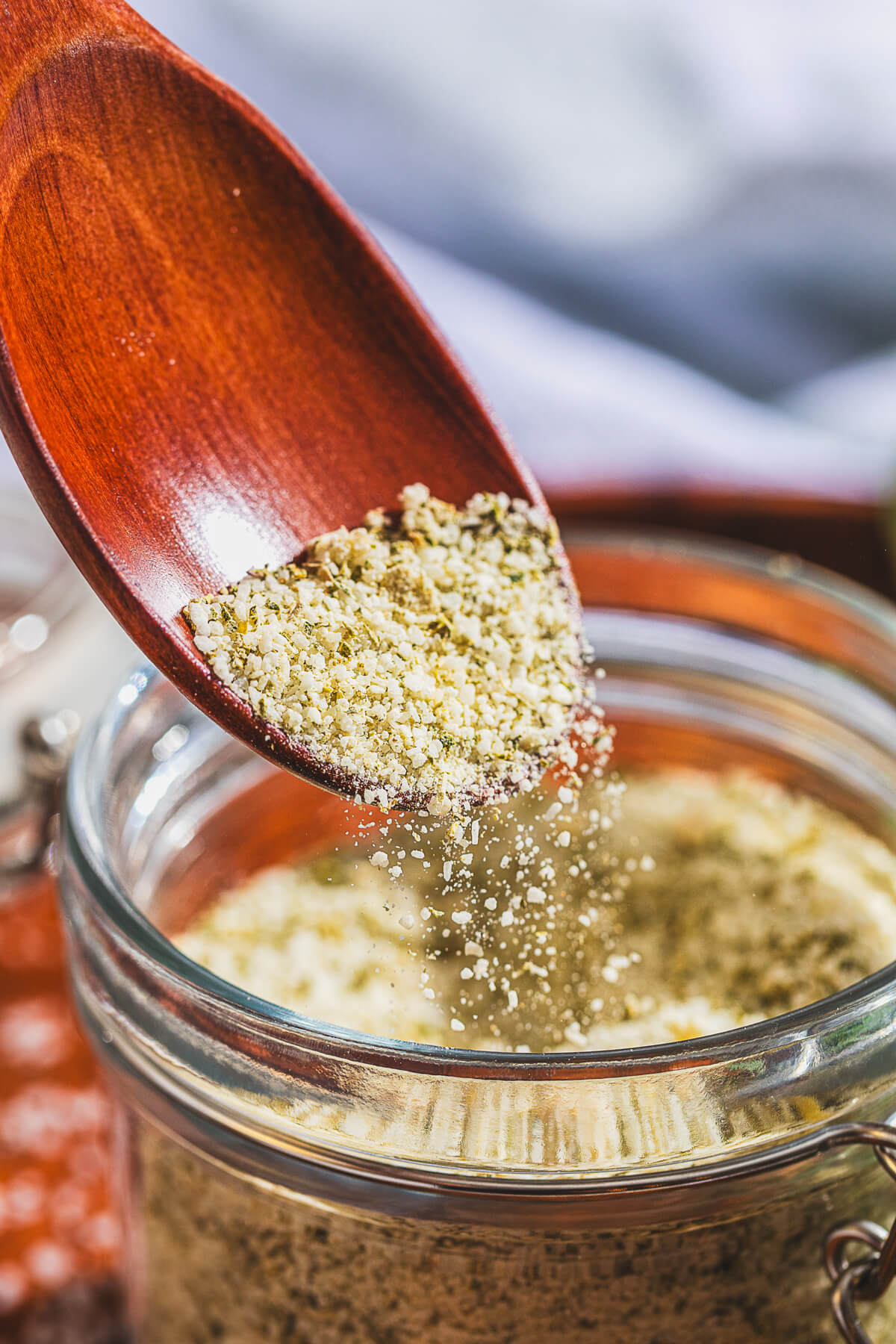 Rosemary Salt pours from a wooden spoon into a glass jar of salt.