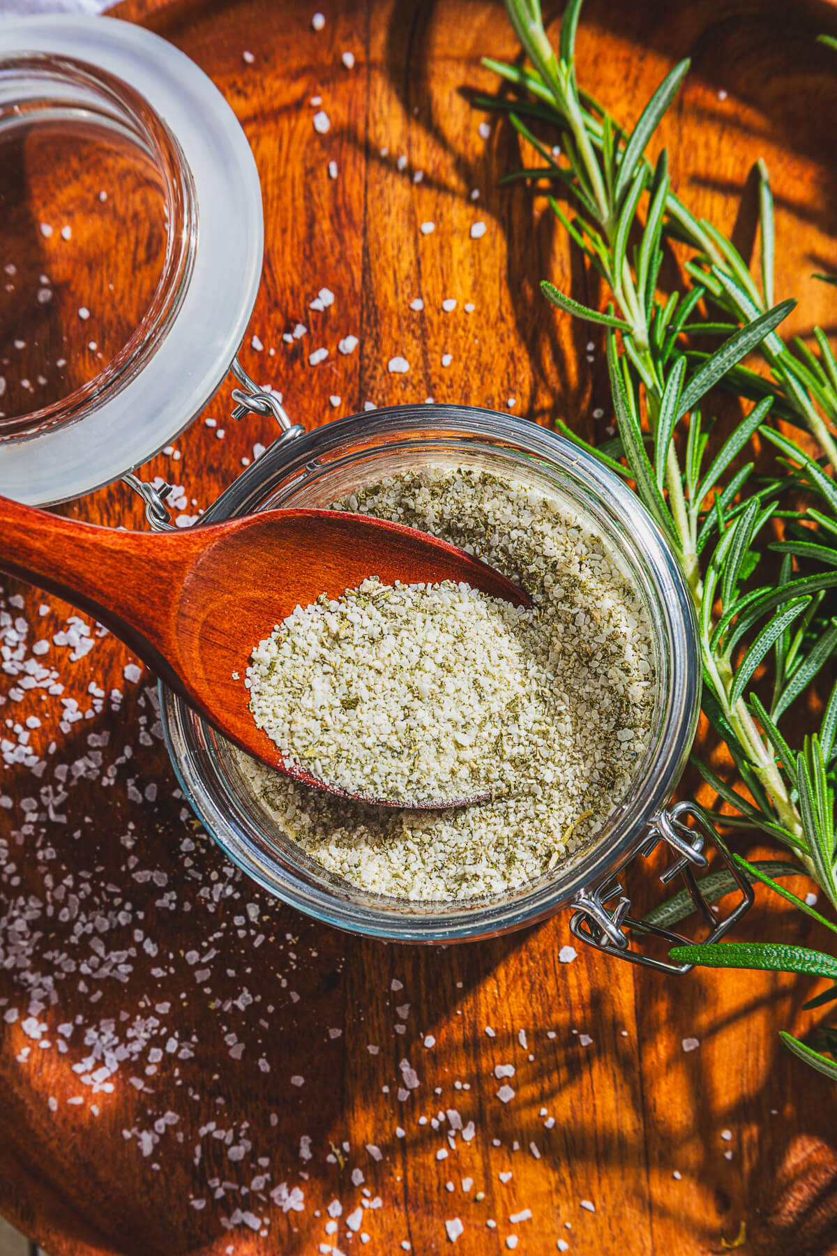 A glass jar of rosemary salt with a wooden spoon in it.