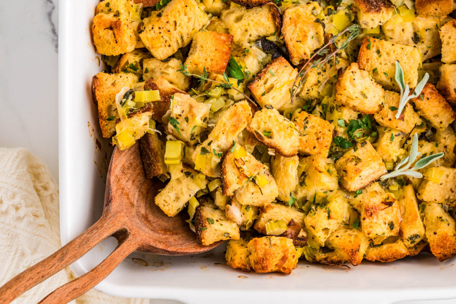 A wooden spoon in a white baking dish full of golden baked Sourdough stuffing.