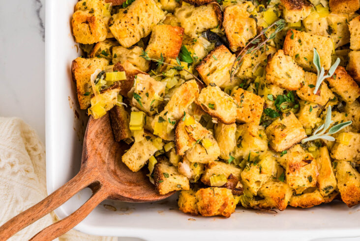 A wooden spoon in a white baking dish full of golden baked Sourdough stuffing.