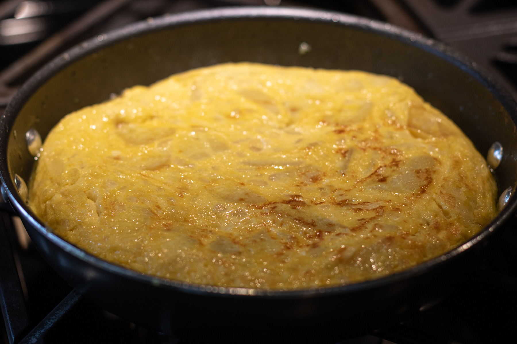 A perfect round yellow Spanish Tortilla or Tortilla de Patatas being cooked in a tortilla pan on a gas stovetop.