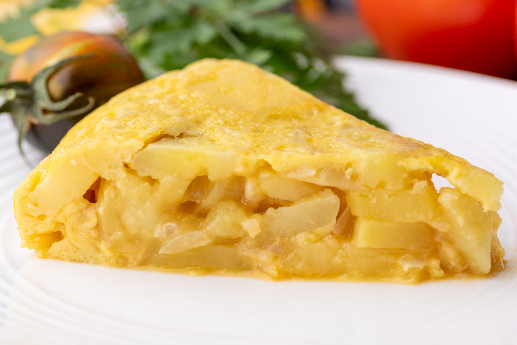A perfect slice of yellow Spanish Tortilla or Tortilla de Patatas on a white plate surrounded by tomatoes.