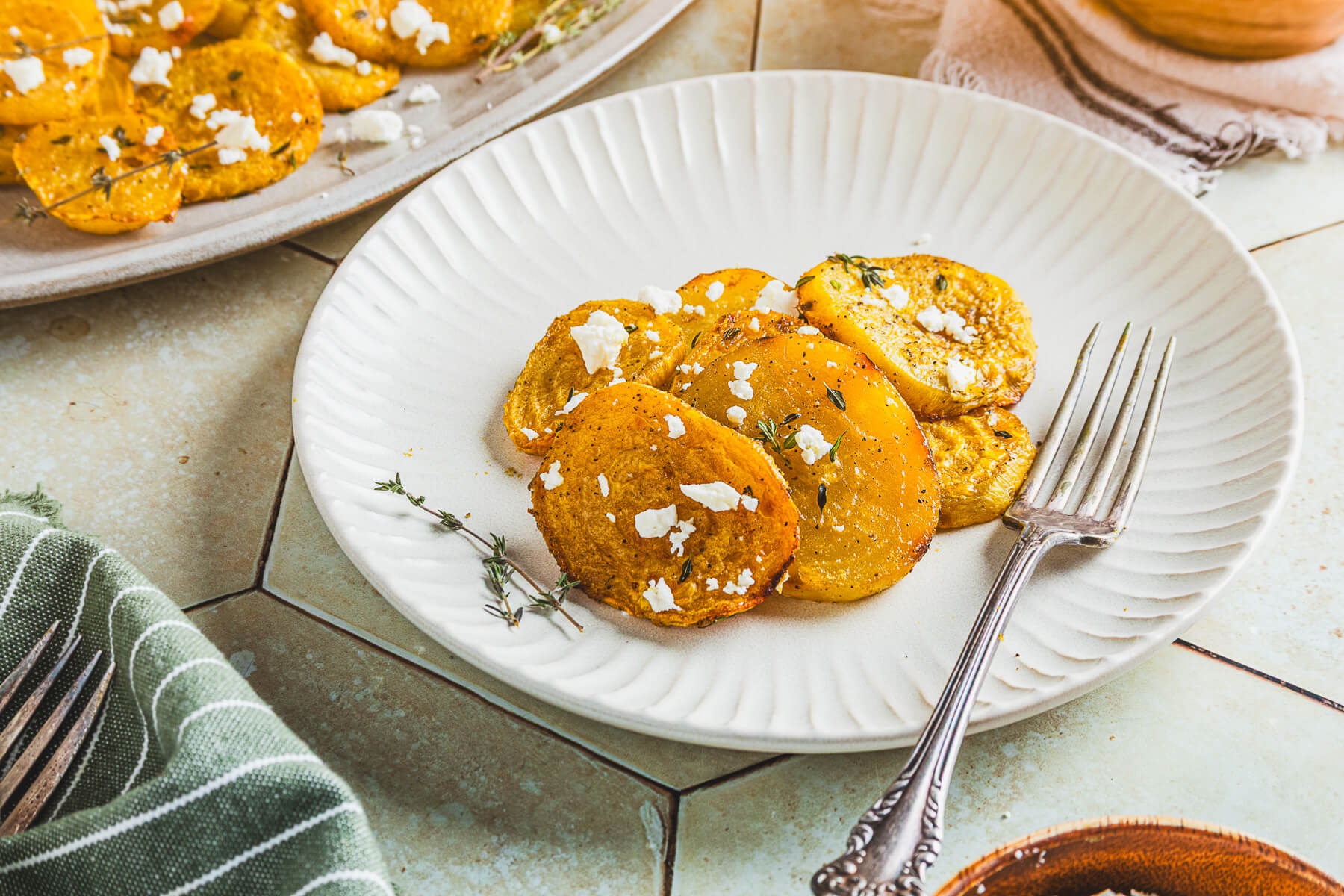 A small white plate containing vibrant roasted golden beets adorned with fresh thyme and crumbled feta on a dinner table.