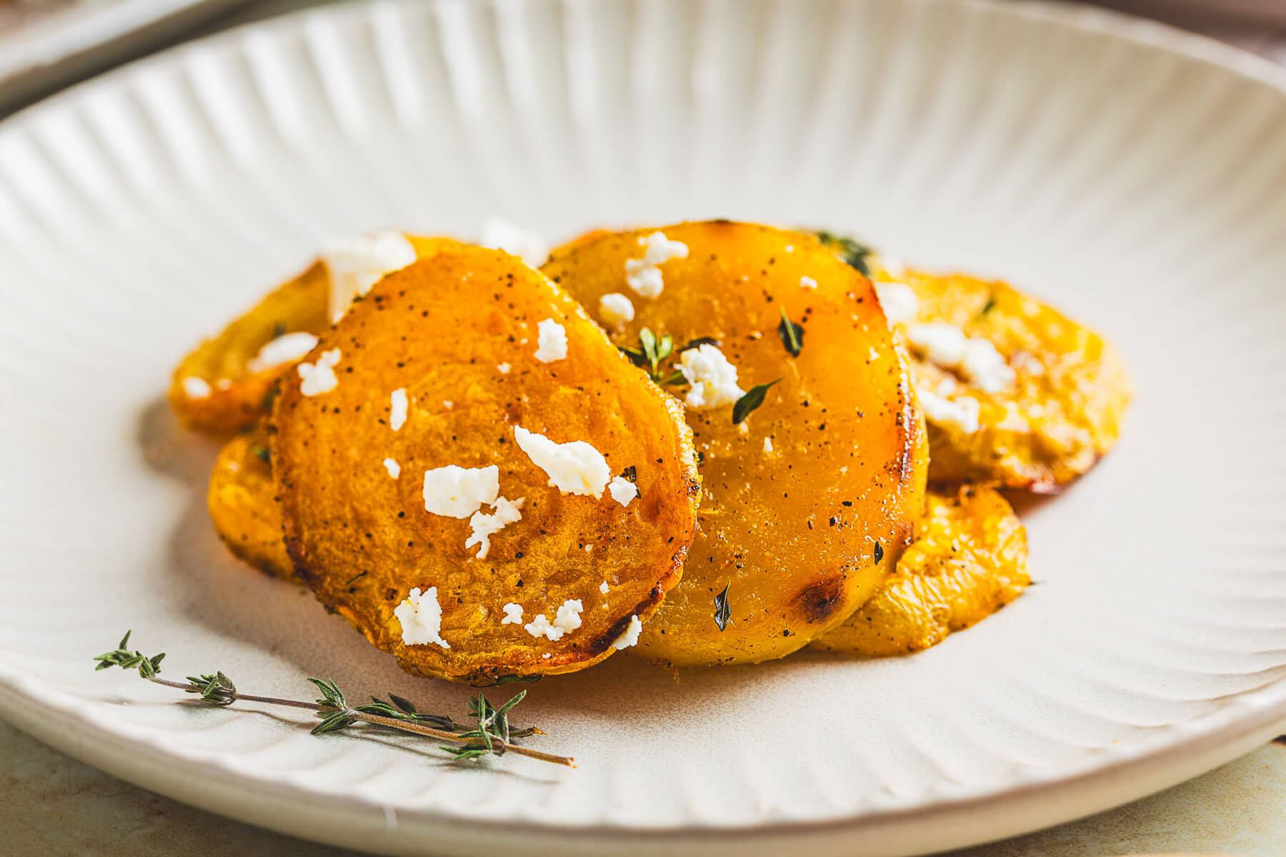 A small white plate containing vibrant roasted golden beets adorned with fresh thyme and crumbled feta on a dinner table.