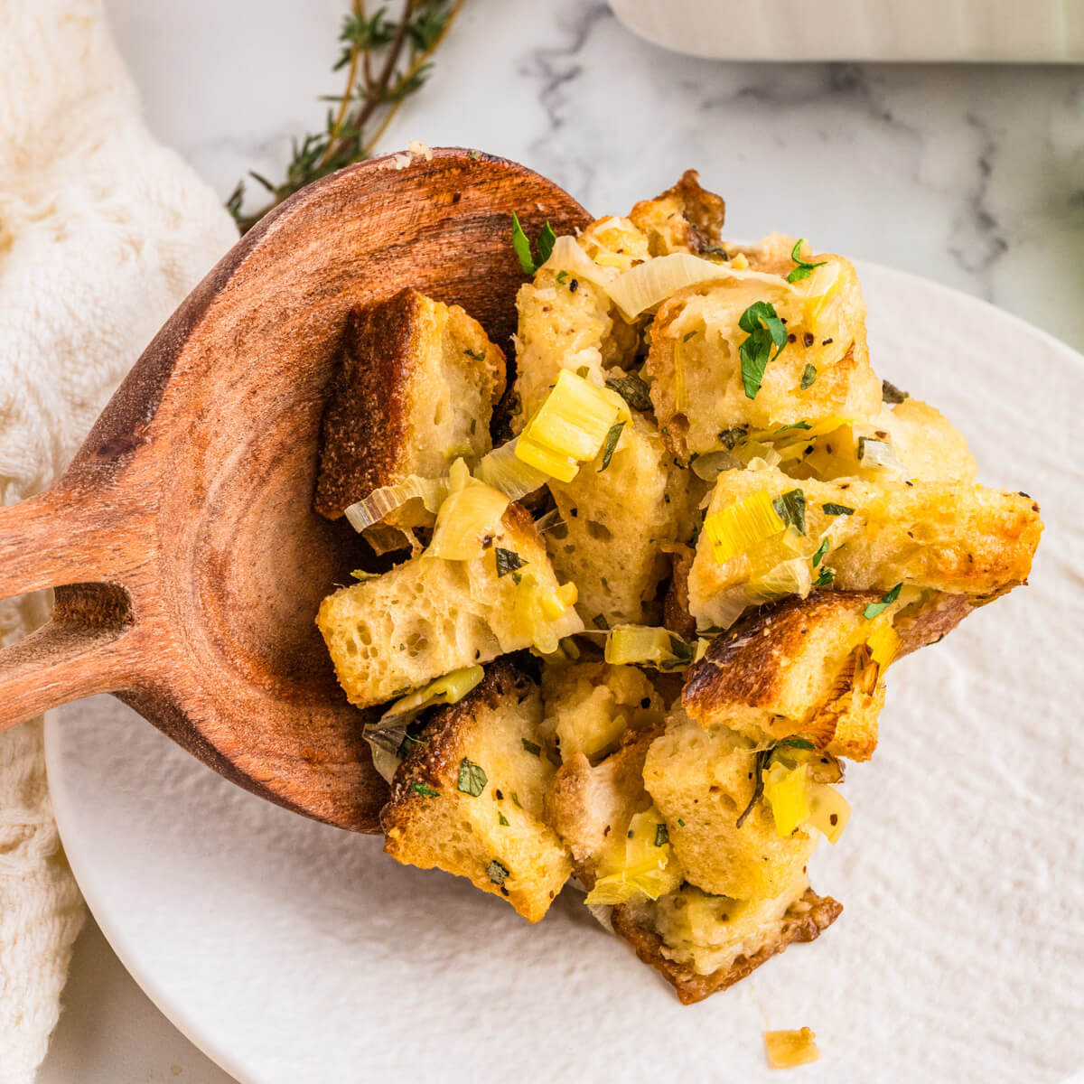 A wooden scoop places golden baked sourdough stuffing on a white plate.