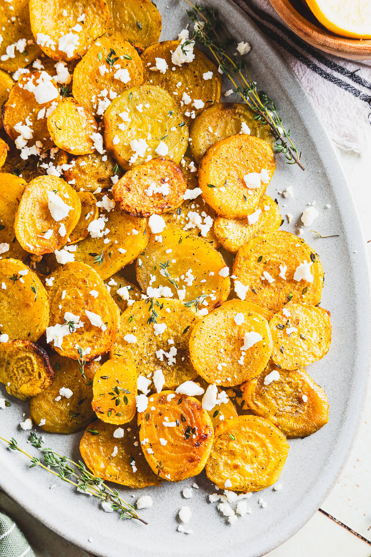 An oval platter containing vibrant roasted golden beets adorned with fresh thyme and crumbled feta