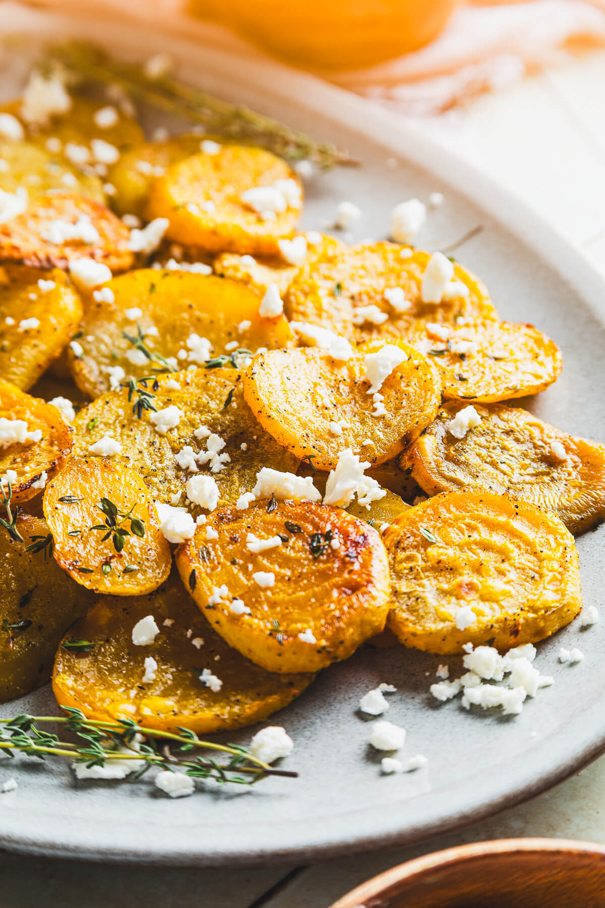 An oval platter containing vibrant roasted golden beets adorned with fresh thyme and crumbled feta on a dinner table.