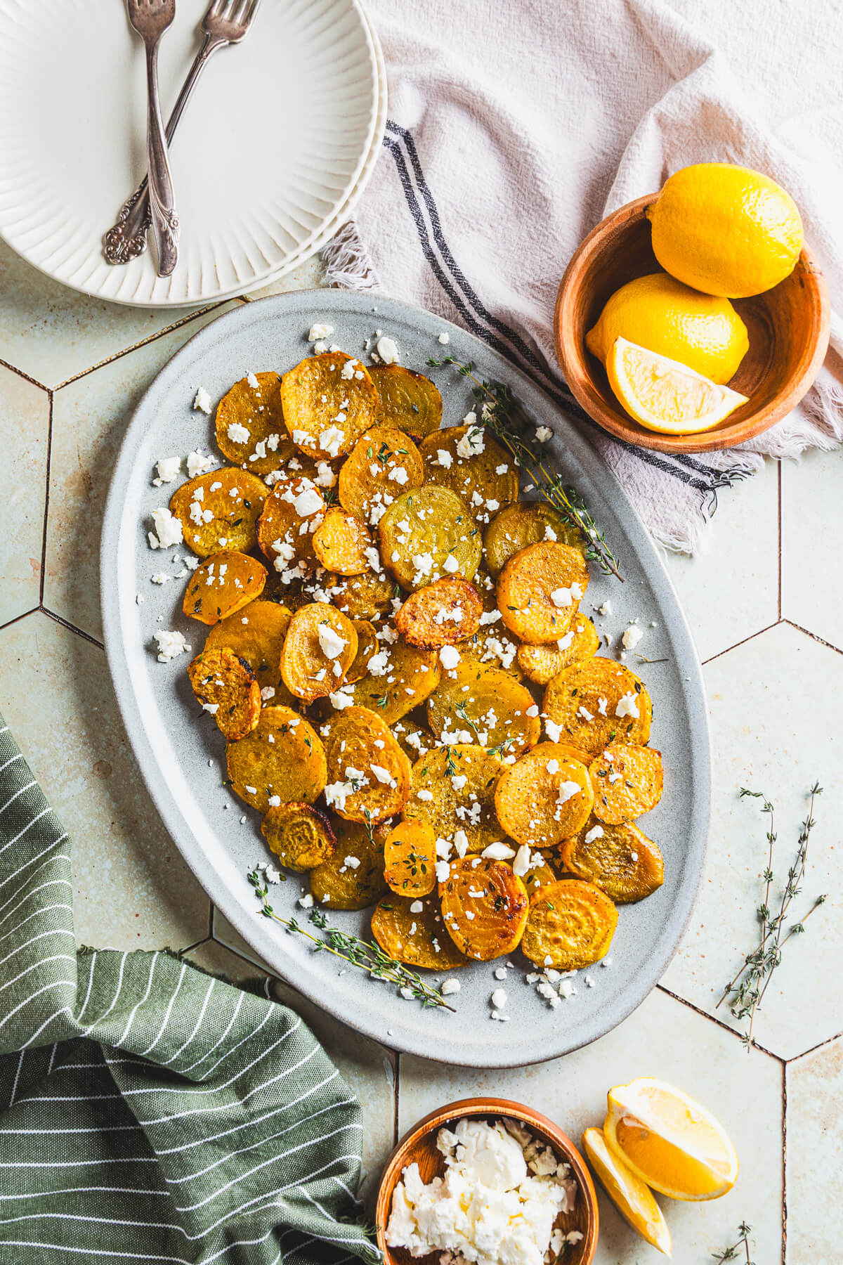 An oval platter containing vibrant roasted golden beets adorned with fresh thyme and crumbled feta on a dinner table.